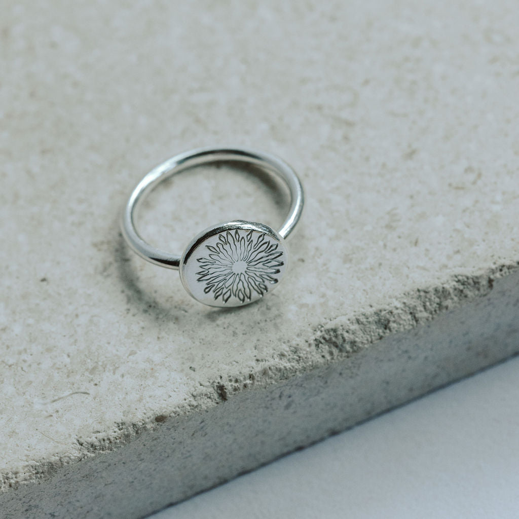 Silver ring with a sunrise design on a stone surface