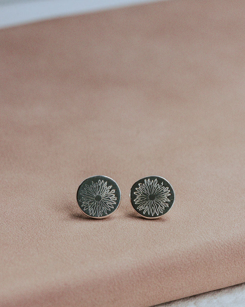 Pair of silver sunrise stud earrings on a pink surface