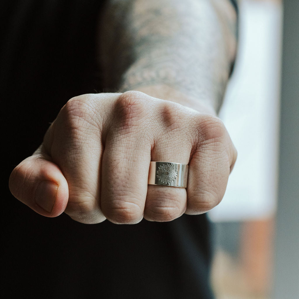 Person wearing a silver ring on a tattooed arm with a blurred background