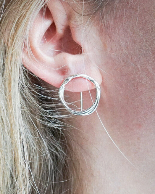 Close-up of a silver hoop earring worn by a person with blonde hair.