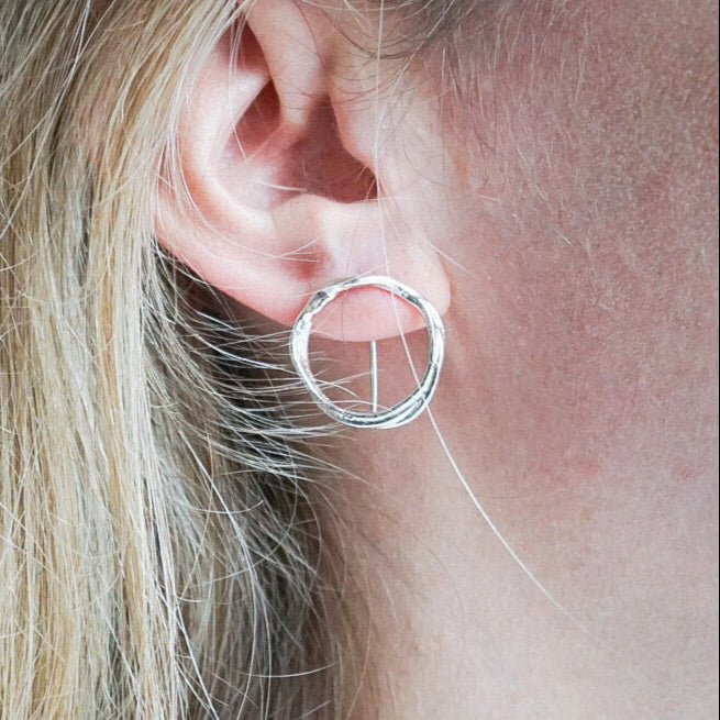 Close-up of a silver hoop earring worn by a person with blonde hair.