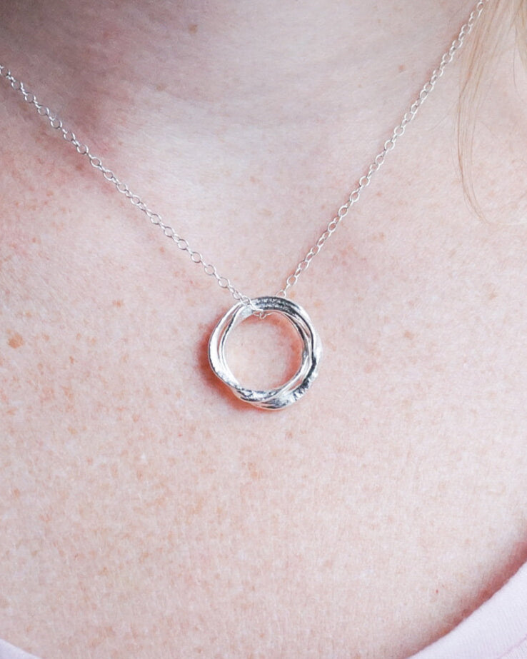 Silver necklace with a interlocking circles pendant on a person wearing a white shirt.