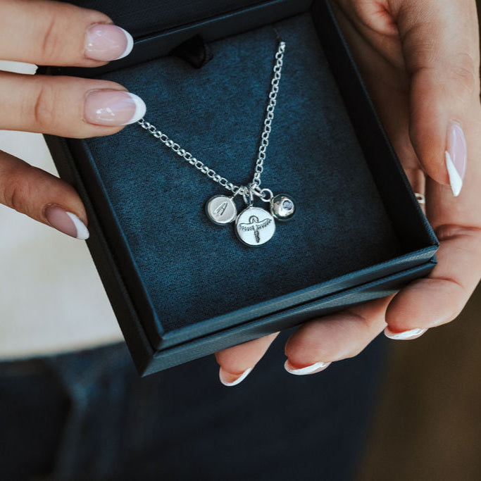 The Phoenix pendant in a dark blue box held in a woman's hands.