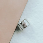 Silver ring with a darling heart design on a light pink and white background