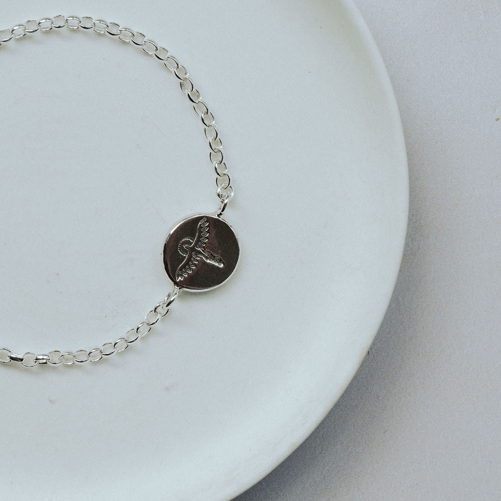 Silver bracelet with a round disc featuring a phoenix on a white plate