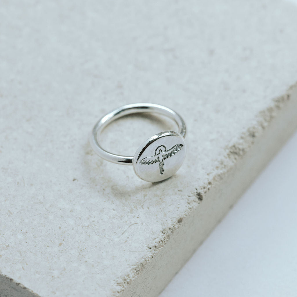 Silver ring with hand stamped phoenix design on a textured stone surface