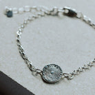 Silver bracelet with a textured round charm on a light stone surface