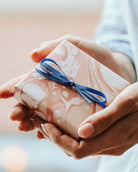 Present wrapped in pink marbled paper held by women.