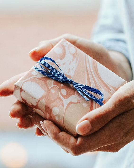 Present wrapped in pink marbled paper held by women.