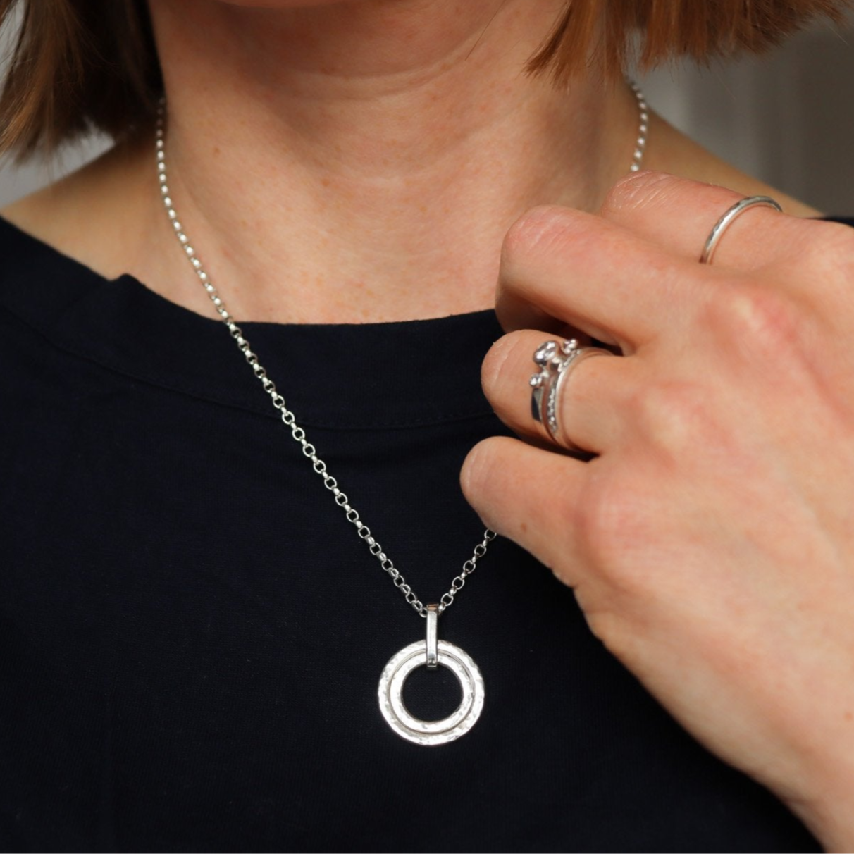 Two textured silver circle pendants nestled together on a silver chain, modelled by Hannah.
