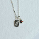Necklace featuring two charms on a white background. One charm has a feather motif and one has a birthstone set in it.