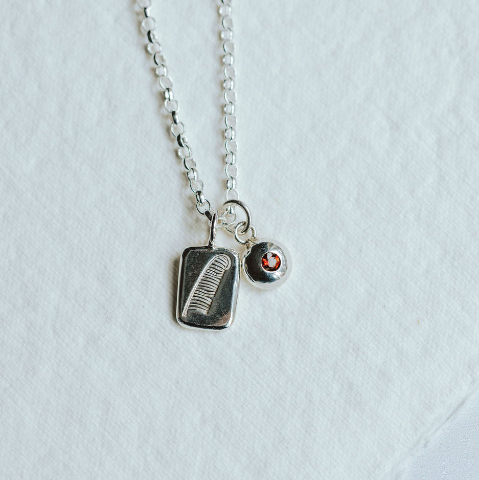 Necklace featuring two charms on a white background. One charm has a feather motif and one has a birthstone set in it.