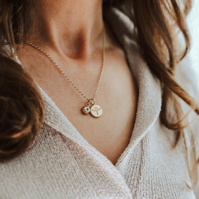 Close-up of a person wearing a delicate gold necklace with Phoenix and birthstone pendants.