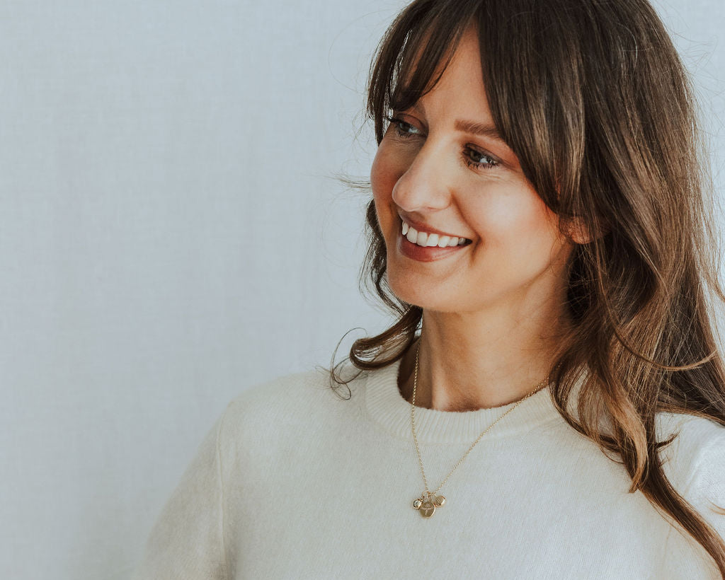 Woman wearing a gold necklace and white t-shirt against a plain background
