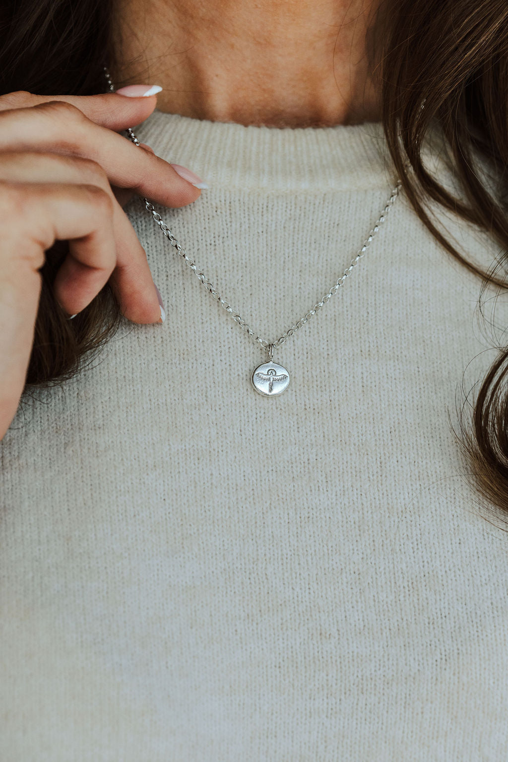Person wearing a necklace with a phoenix pendant on a neutral background