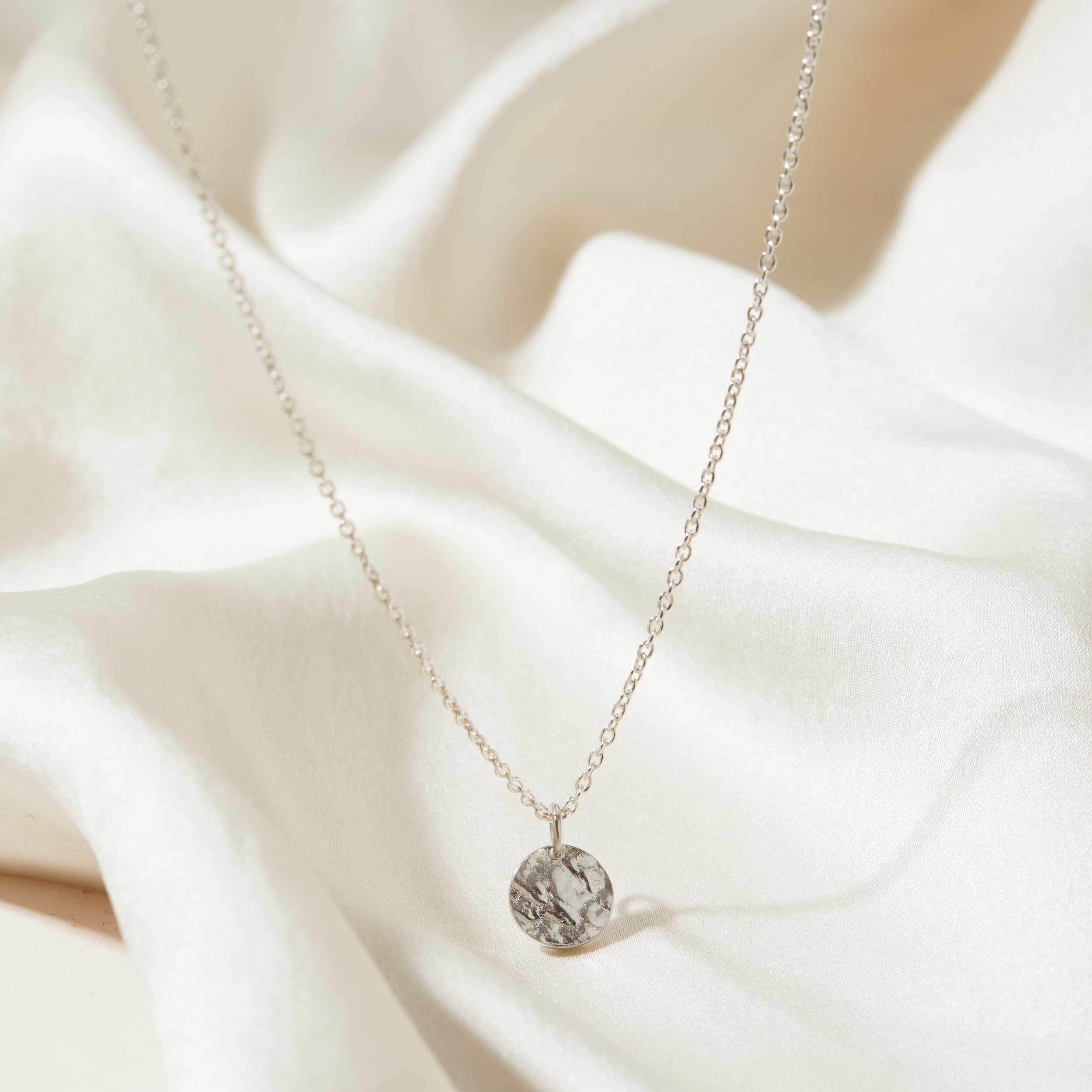 Silver necklace with a tree textured pendant on a white fabric background