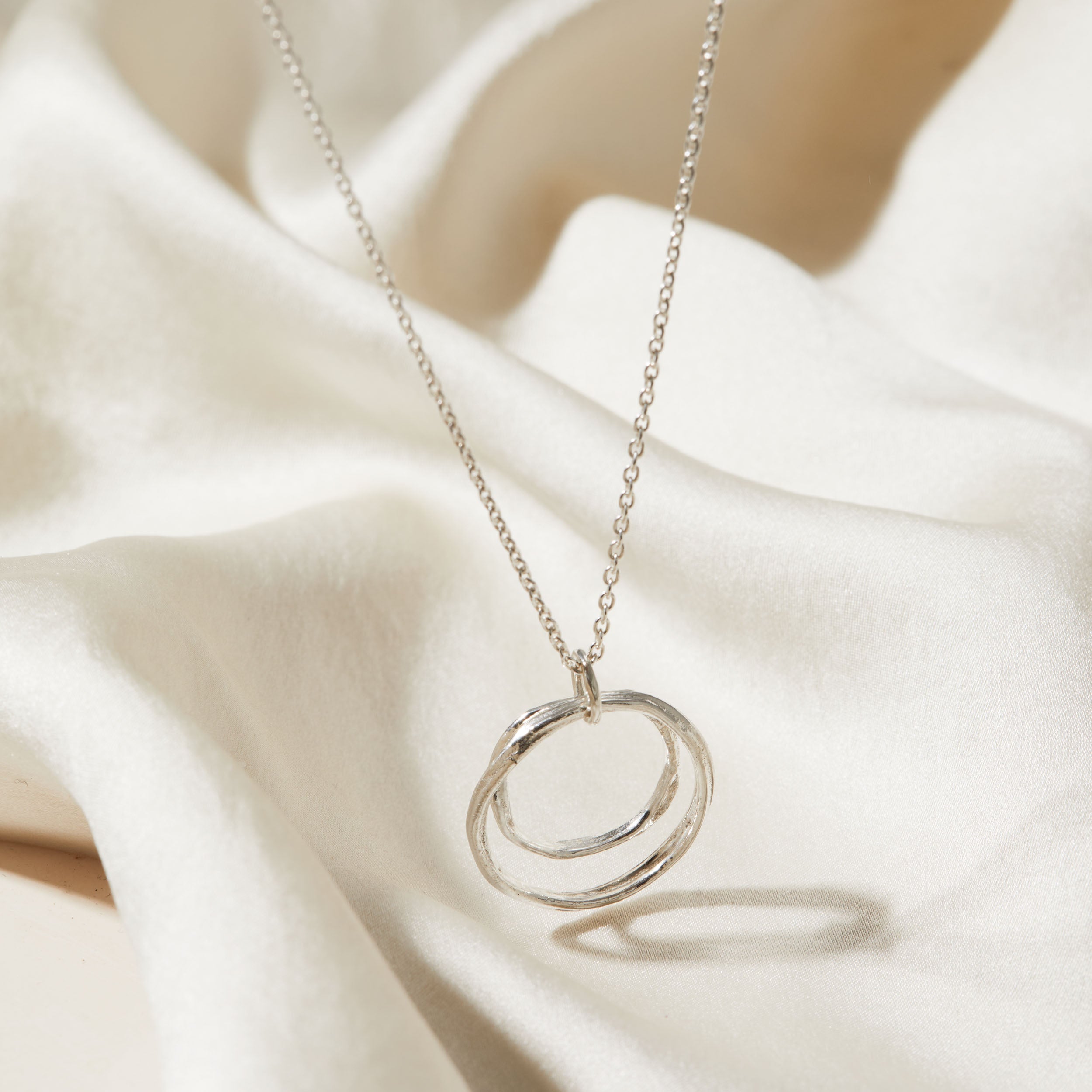 Silver necklace with a double-circle pendant on a soft beige fabric background