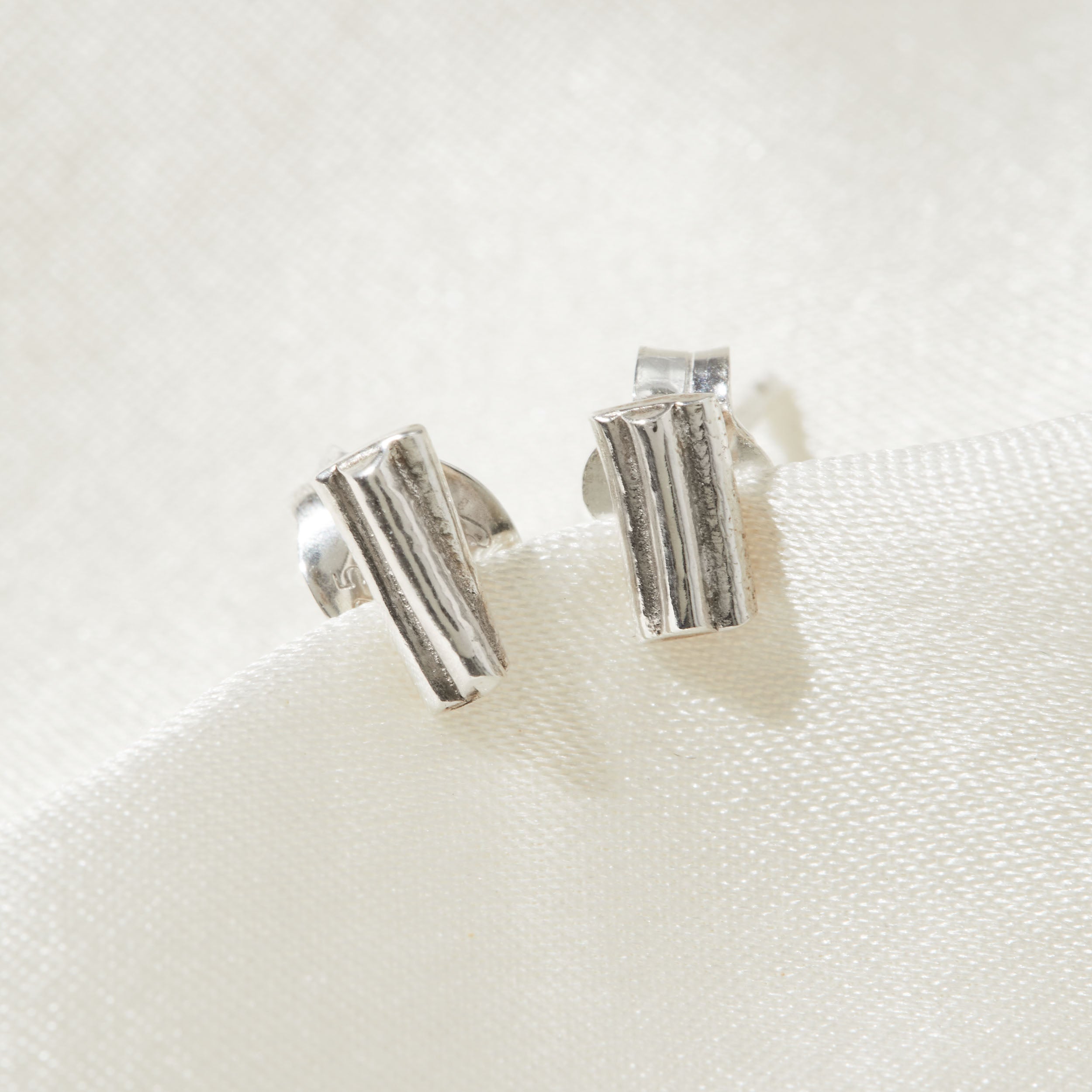Silver ripple stud earrings on a white fabric background