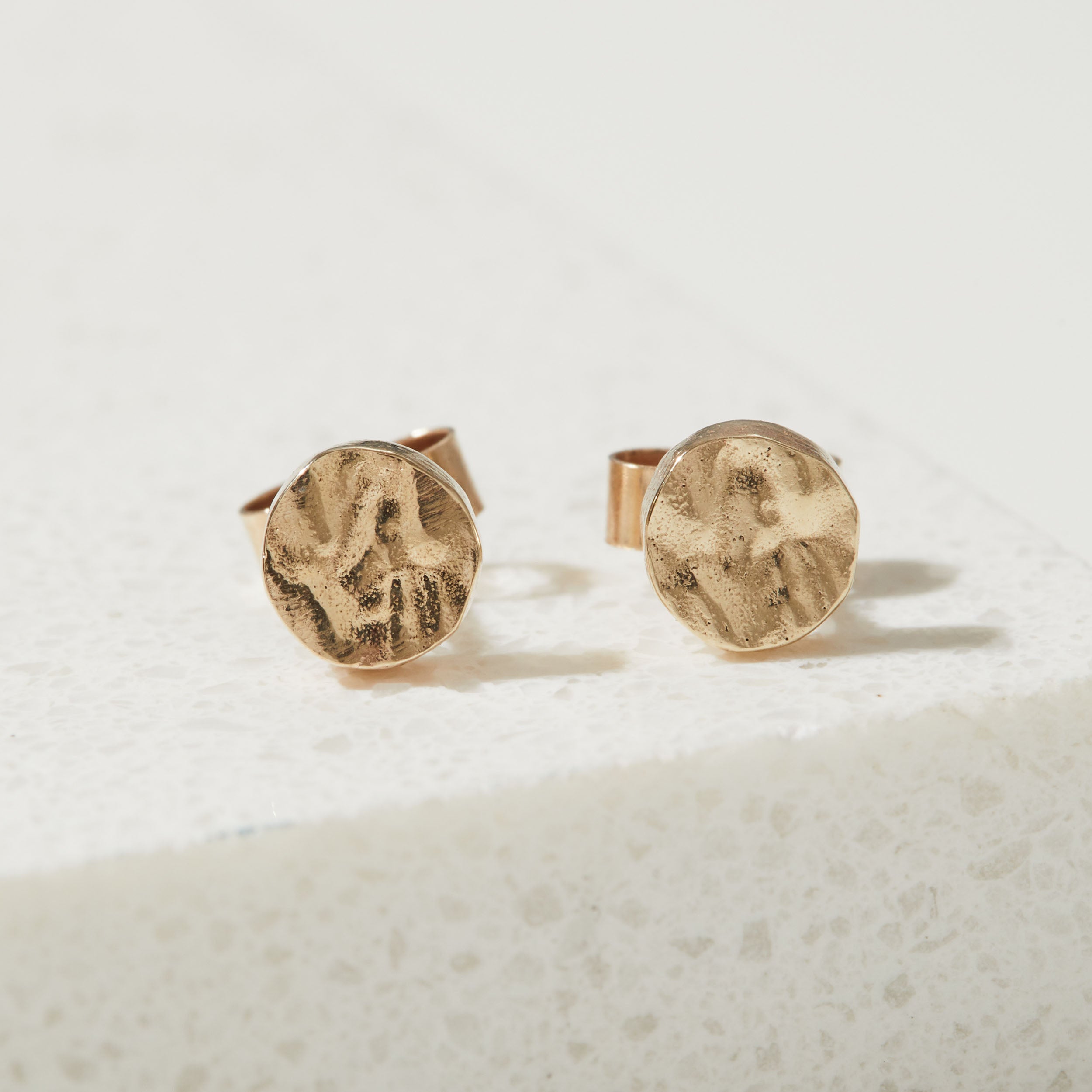 Pair of gold round bark textured stud earrings on a light beige background