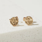 Pair of gold round bark textured stud earrings on a light beige background