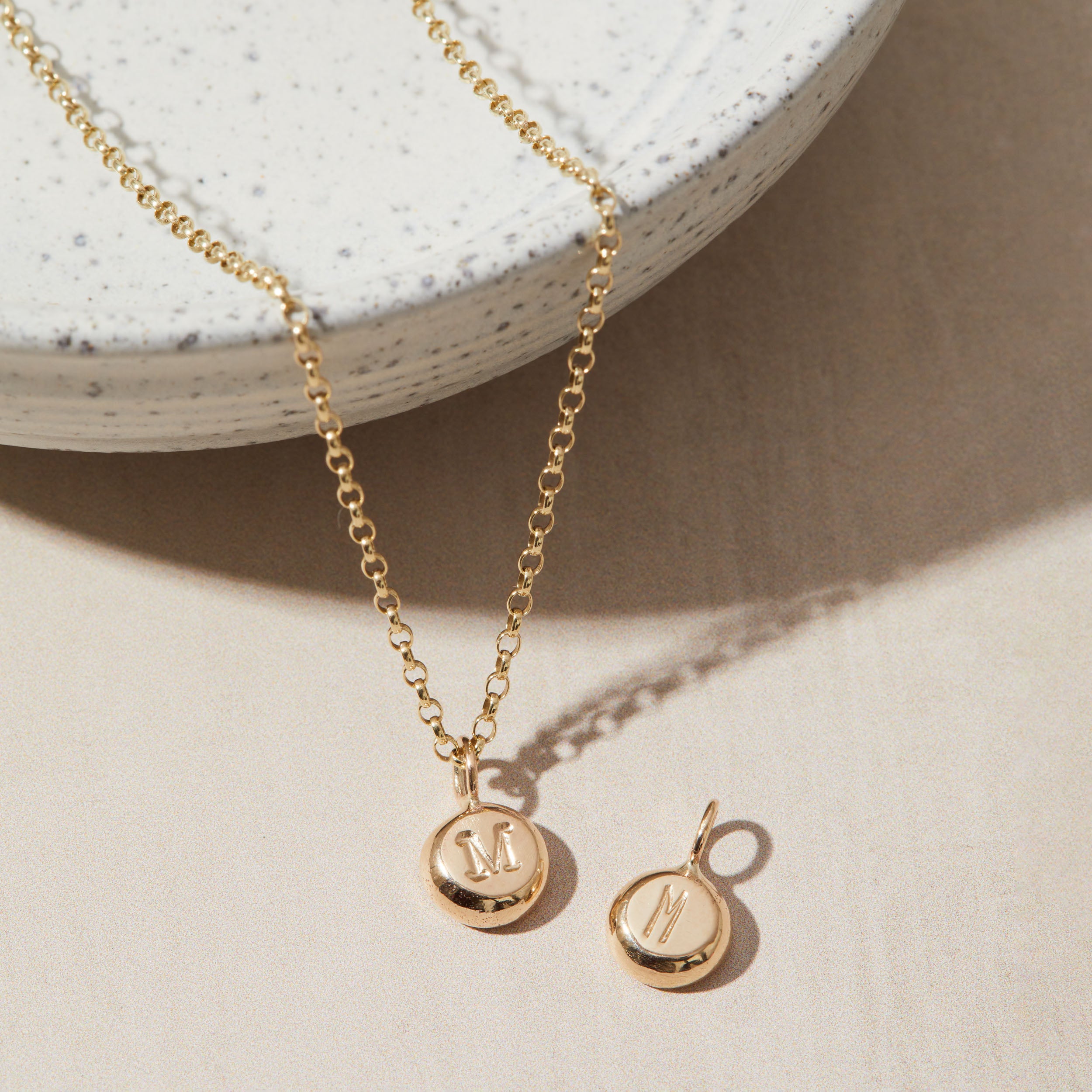 Gold necklace and pendant with 'M' charm on a neutral background
