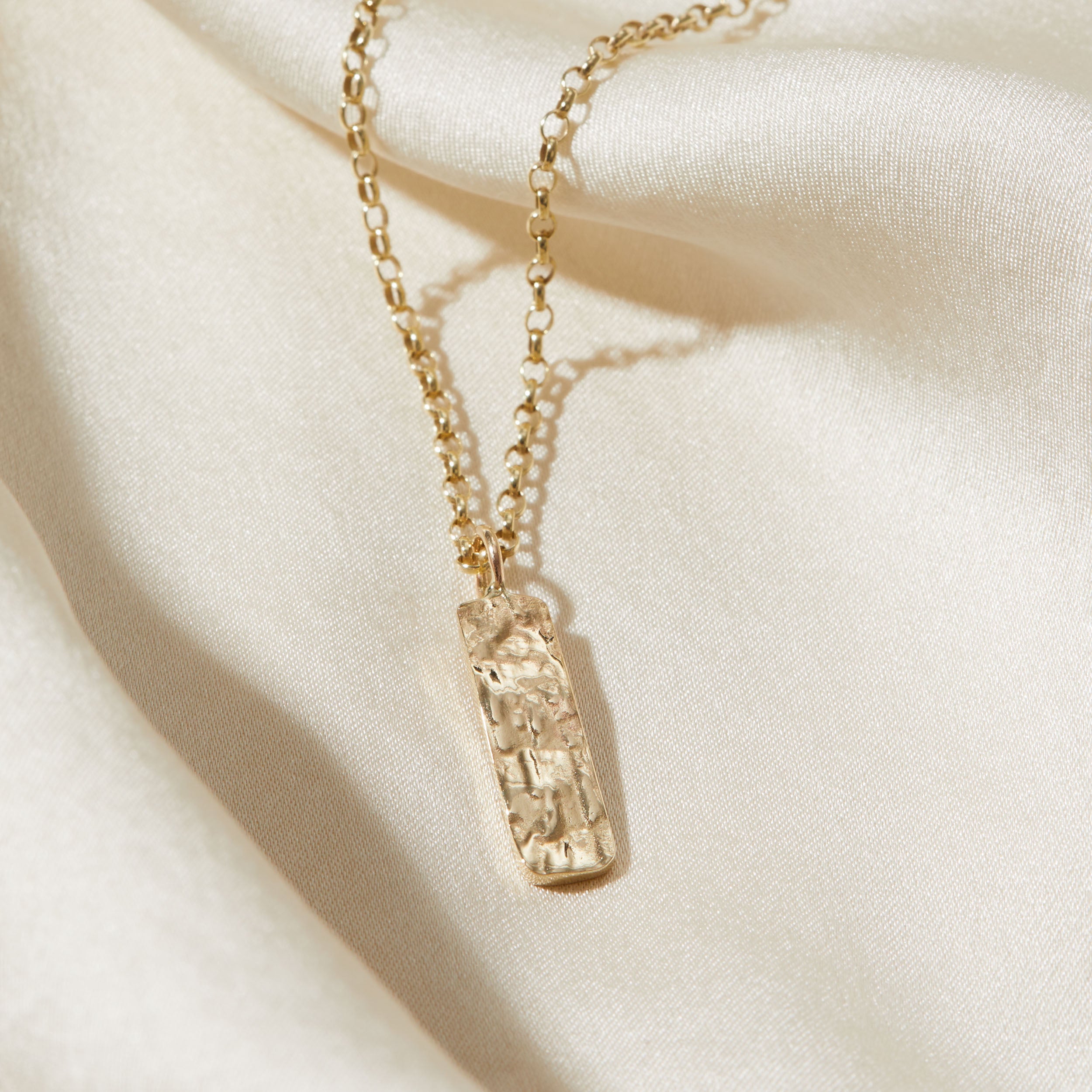 Gold necklace with a bark textured pendant on a beige fabric background