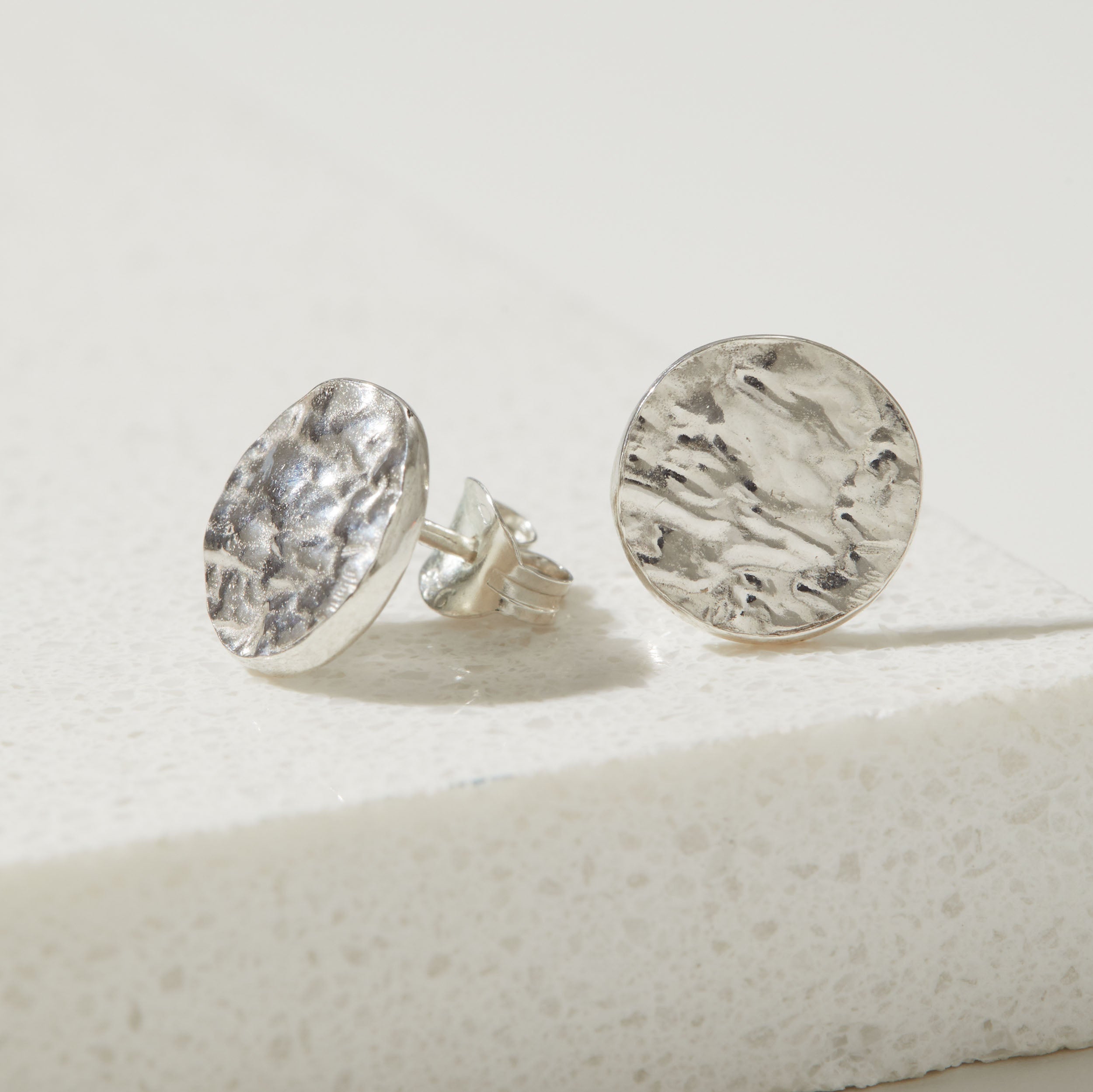 Pair of silver bark textured round earrings on a light gray background