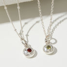 Two silver necklaces with gemstone pendants on a light background