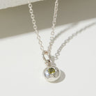 Silver necklace with a pendant featuring a green gemstone on a light background