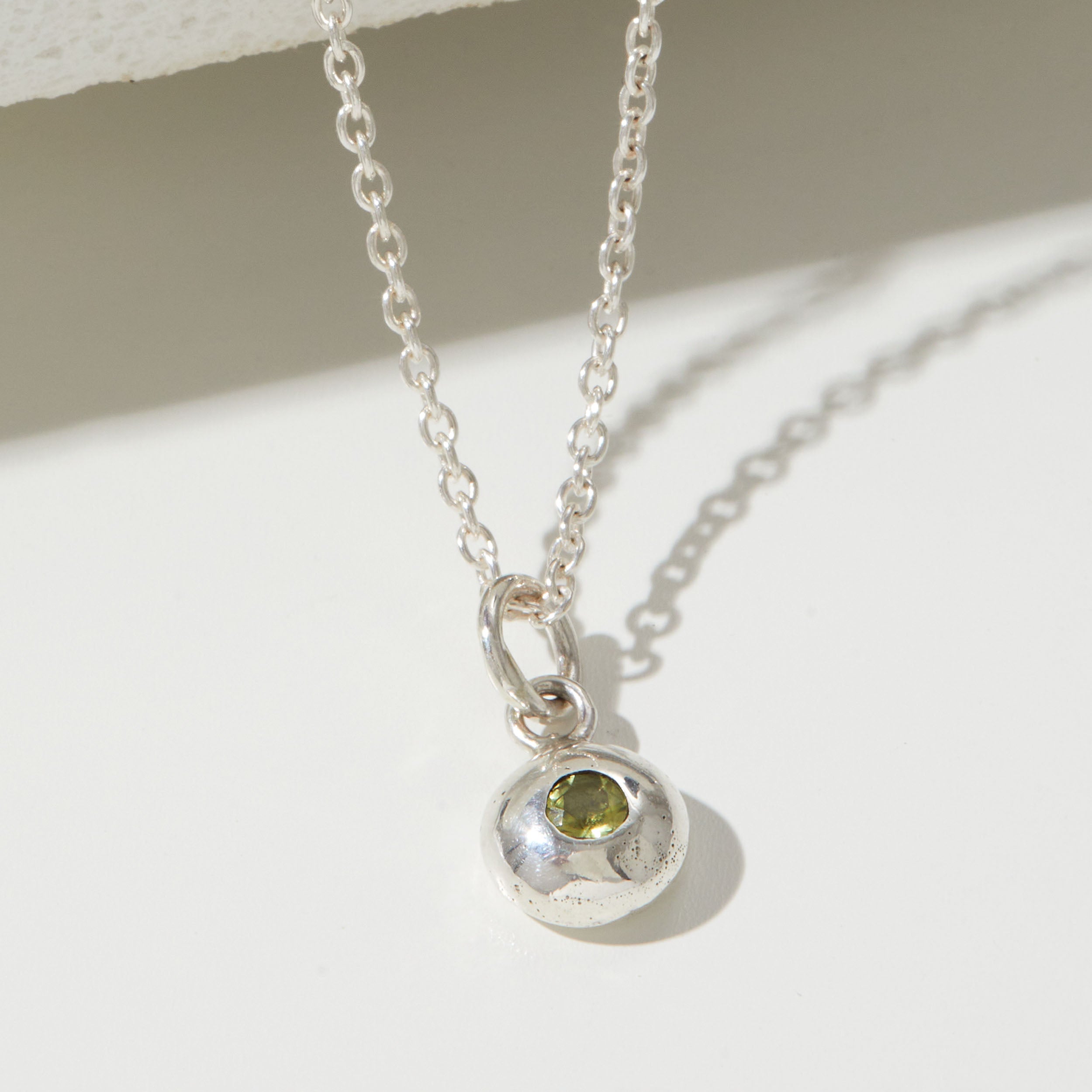 Silver necklace with a pendant featuring a green gemstone on a light background