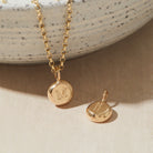 Gold necklace with a pendant featuring the letter 'M' on a neutral background