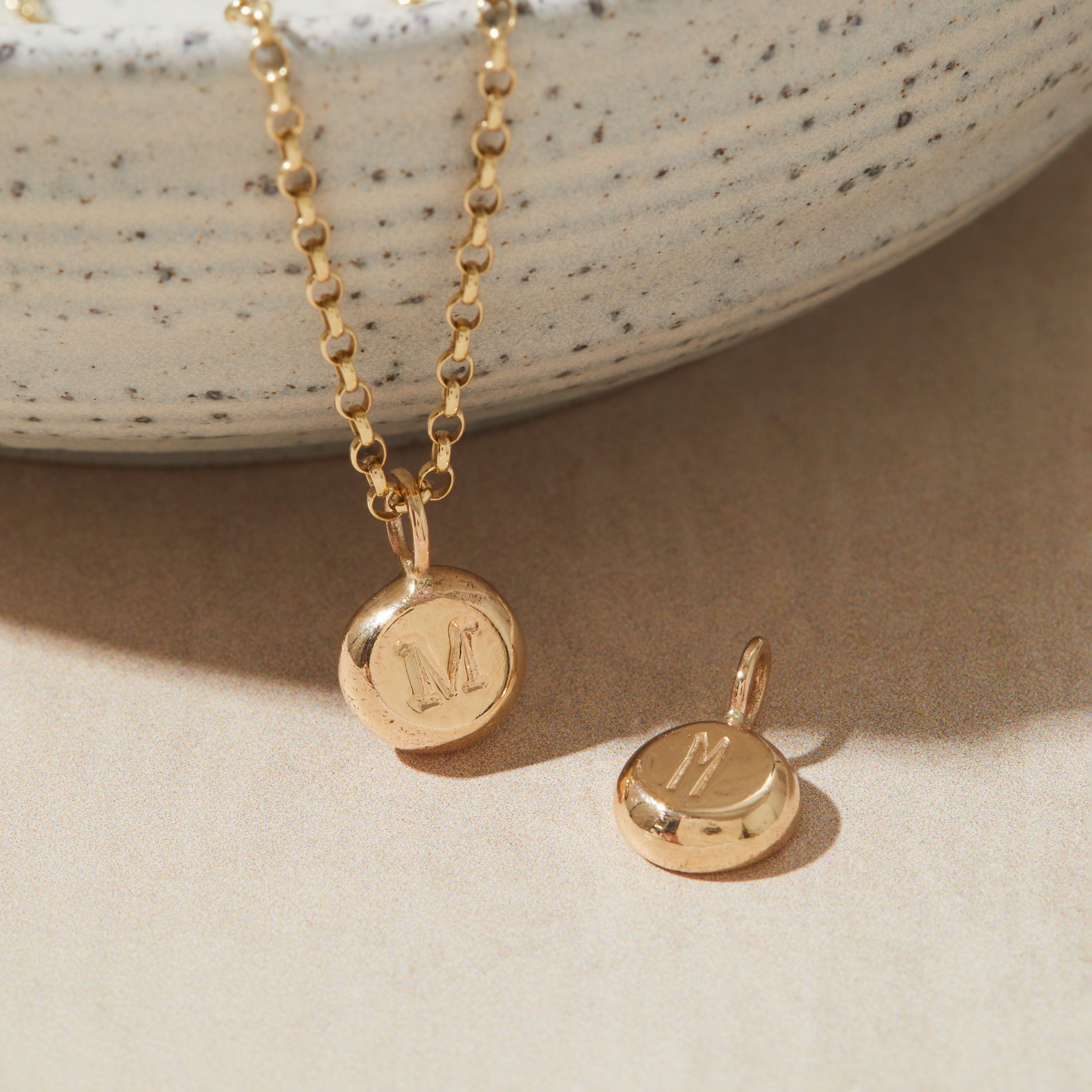 Gold necklace with a pendant featuring the letter 'M' on a neutral background