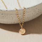 Gold necklace with a round pendant featuring the letter 'M' on a neutral background