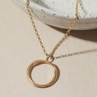 Gold necklace with a circular pendant on a beige surface
