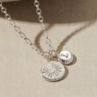 Silver necklace with heart and initial pendants on a beige background