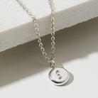 Silver necklace with a round pendant featuring the letter 'S' on a light background