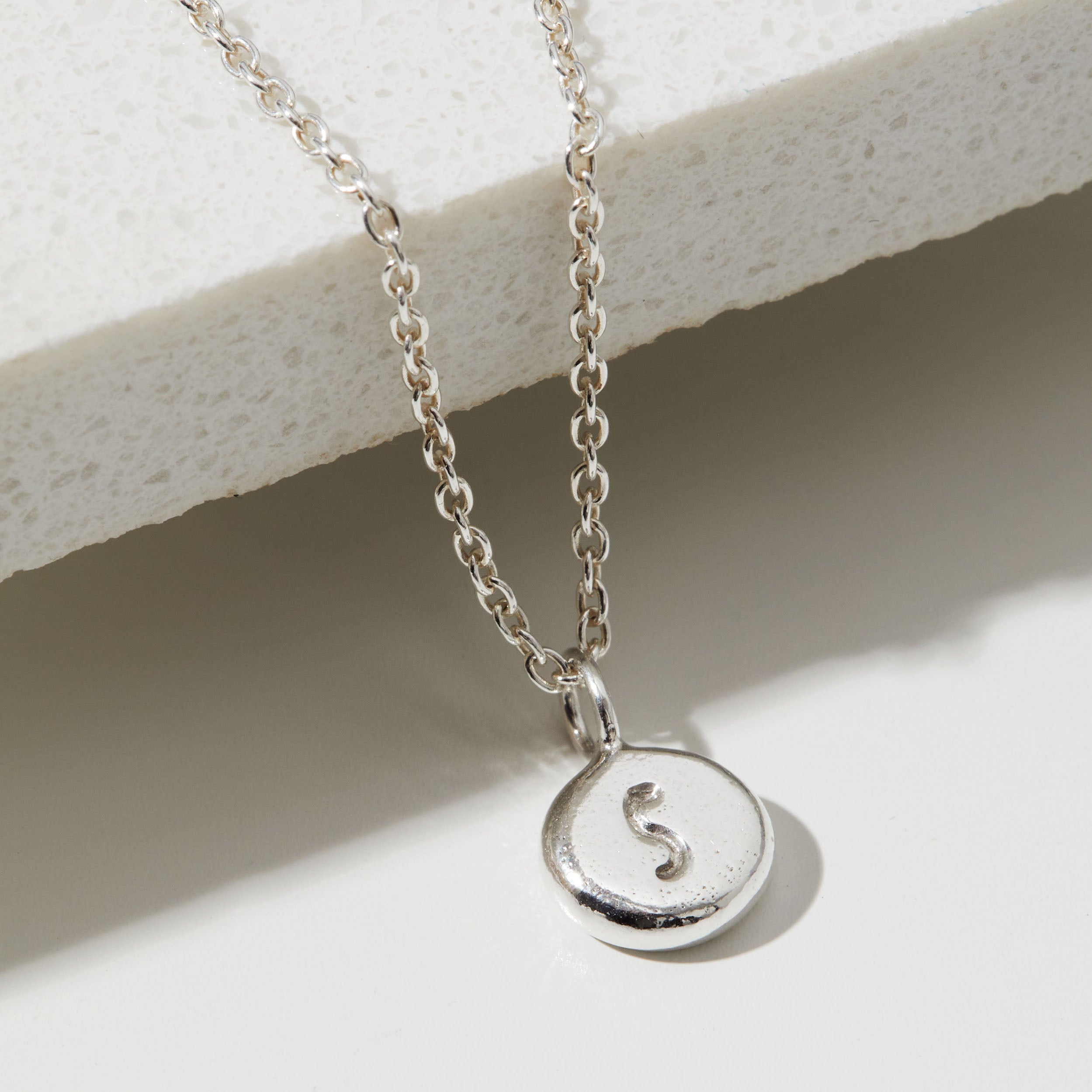 Silver necklace with a round pendant featuring the letter 'S' on a light background