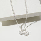 Two silver necklaces with round pendants on a white surface