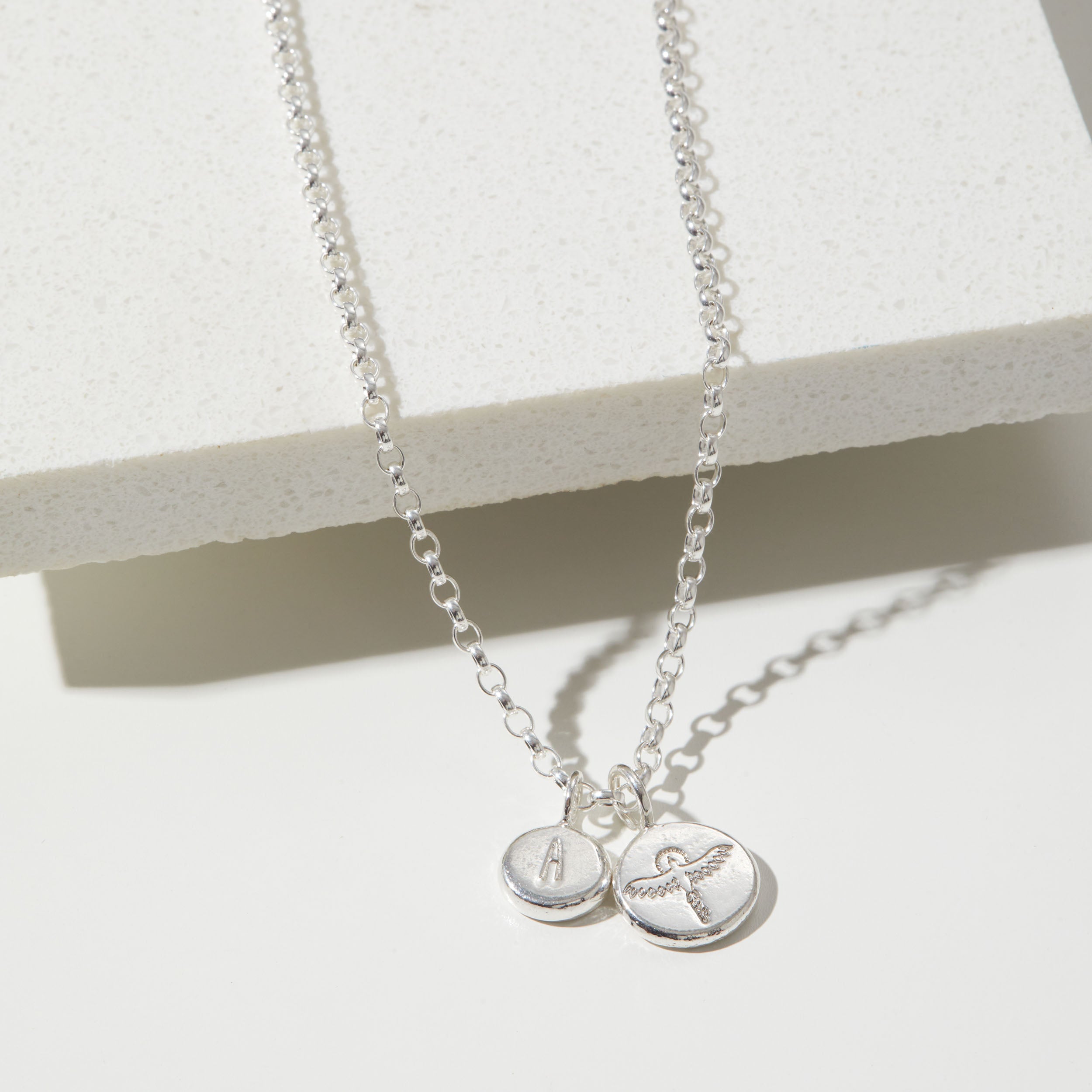 Two silver necklaces with round pendants on a white surface