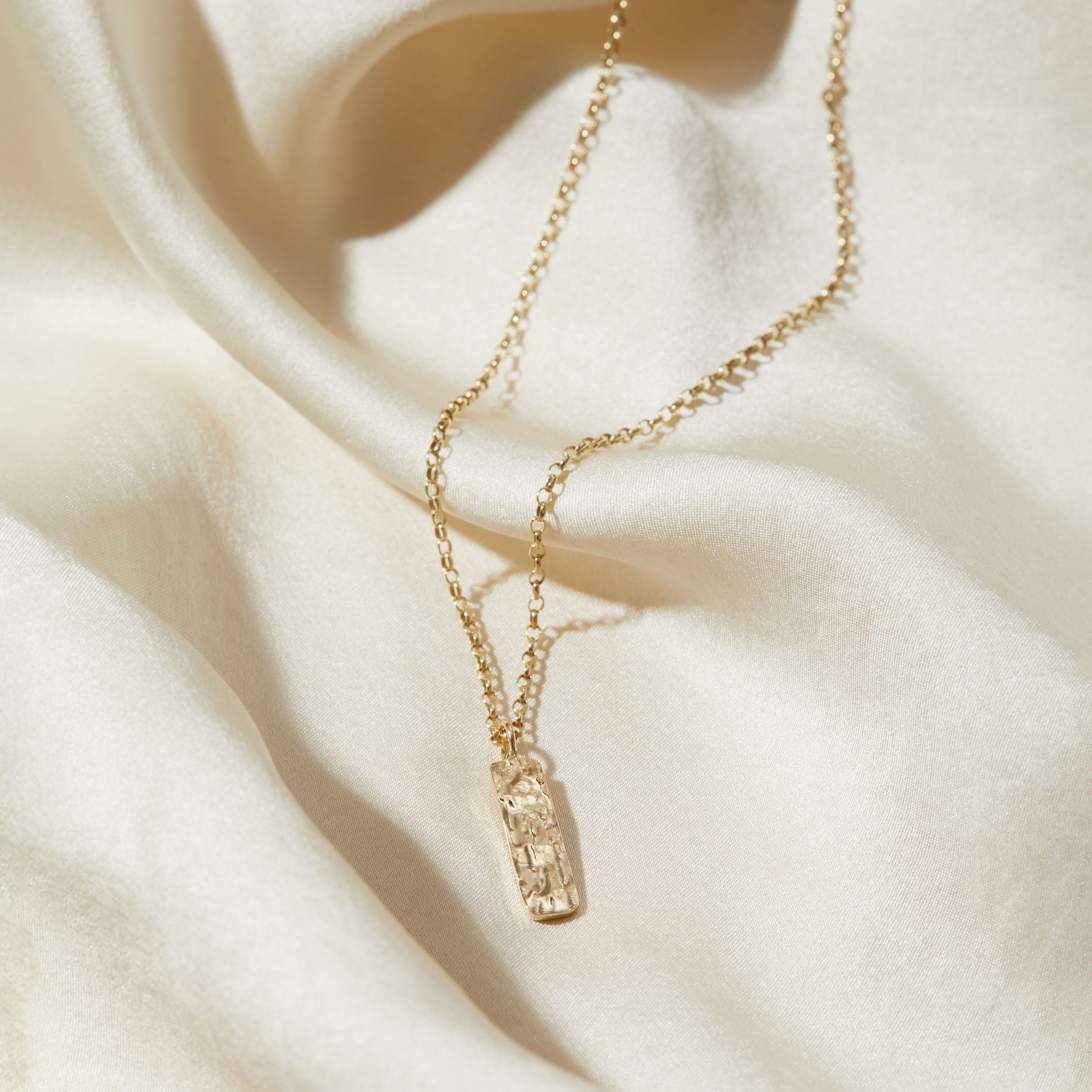 Gold necklace with a bark textured pendant on a beige fabric background