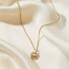 Gold necklace with a bark textured pendant on a soft beige fabric background