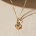 Gold necklace with a gemstone pendant featuring a gemstone on a beige background