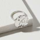 Silver ring with a bark textured circular design on a light background