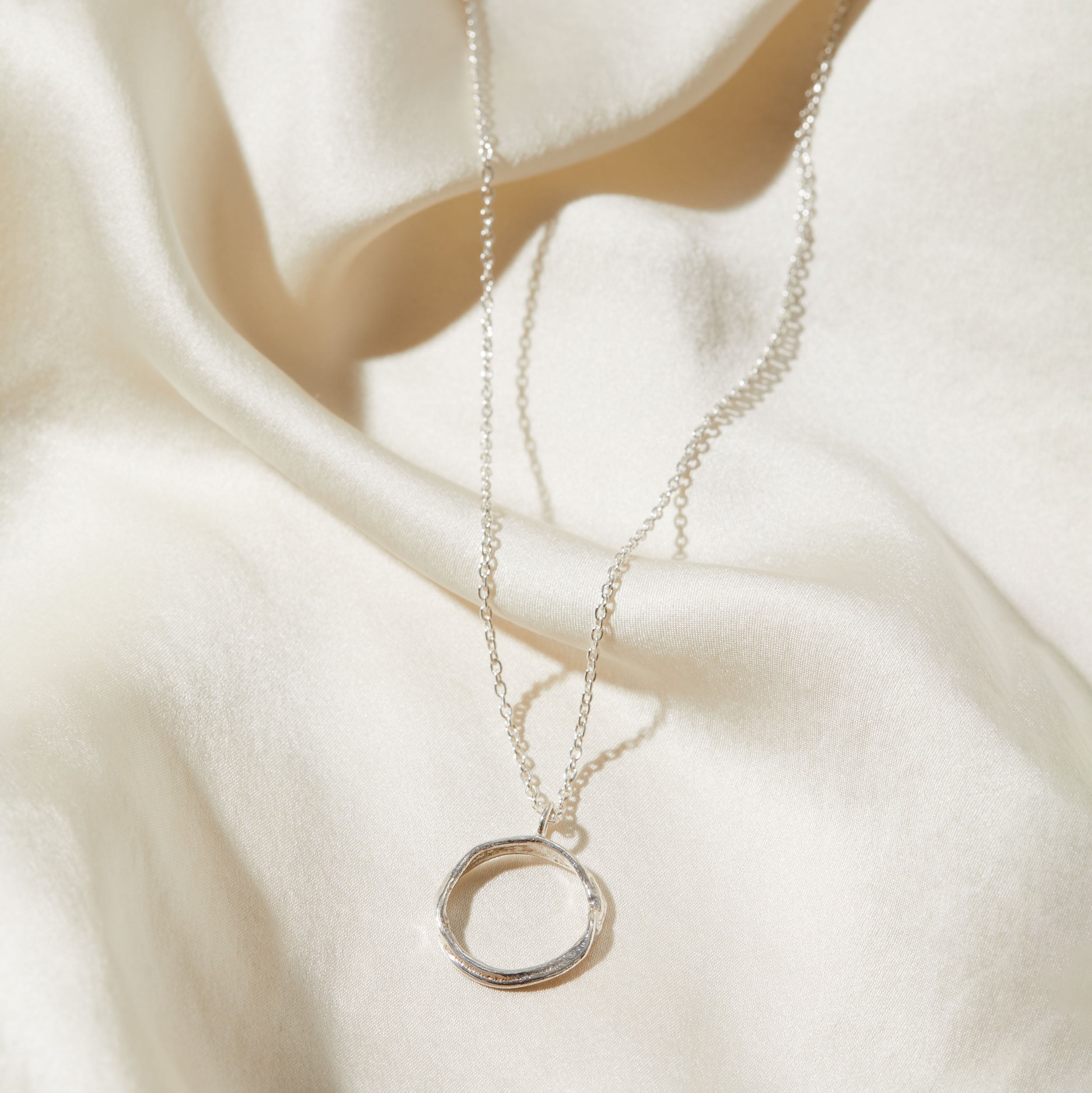 Silver necklace with a circular pendant on a white fabric background