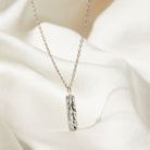 Silver necklace with a bark texture pendant on a white fabric background