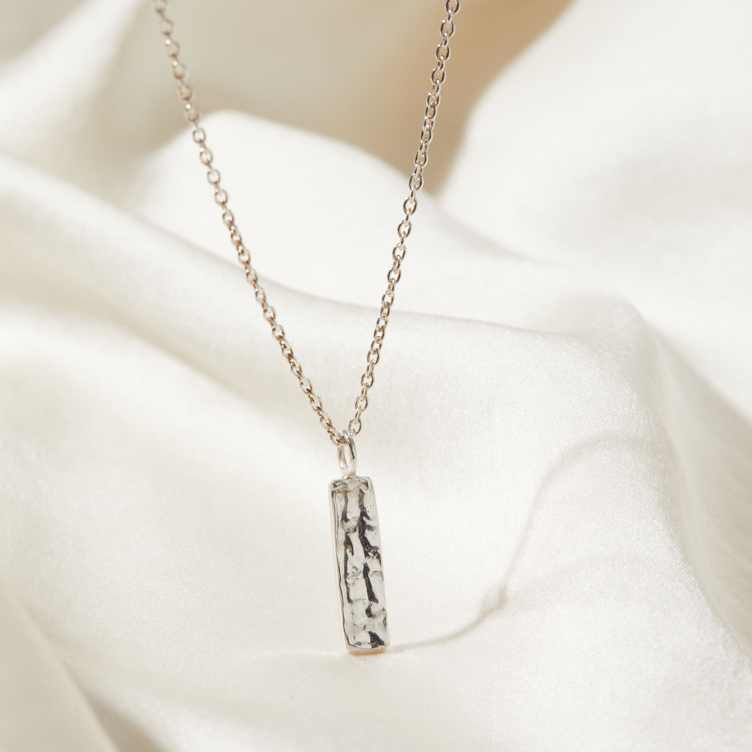 Silver necklace with a bark texture pendant on a white fabric background