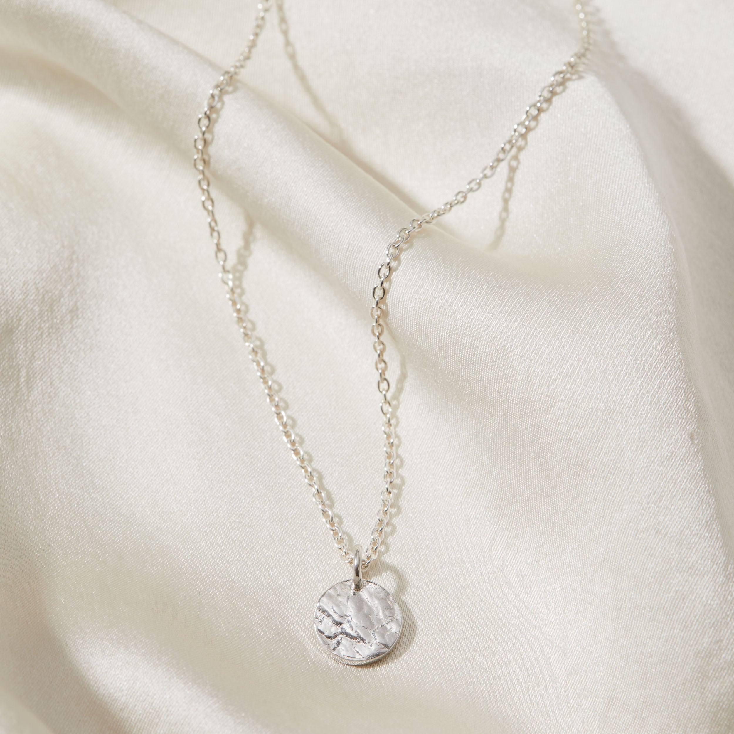 Silver necklace with a bark textured pendant on a soft beige fabric background