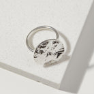 Silver ring with a bark textured circular design on a light gray background