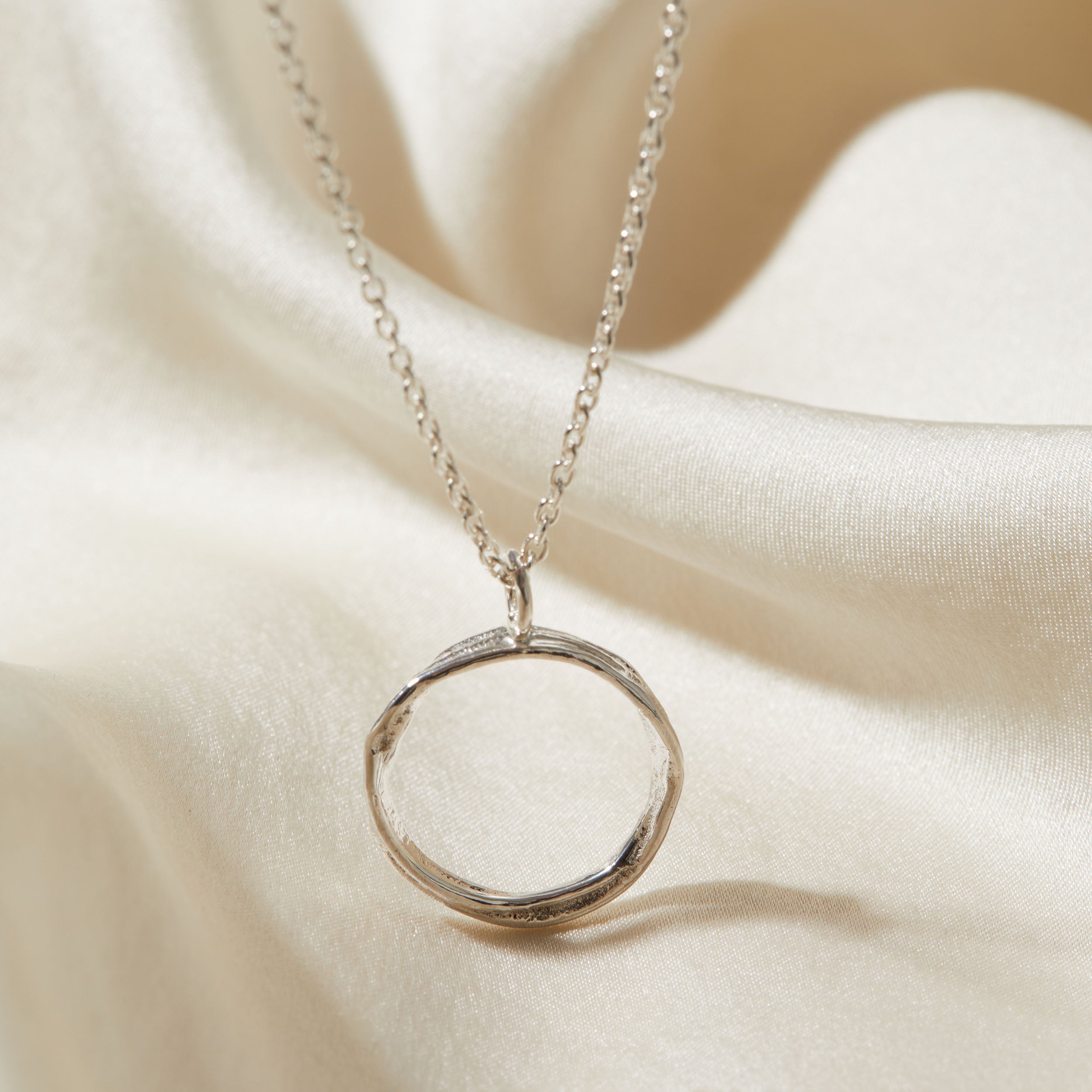 Silver necklace with a circular pendant on a beige fabric background