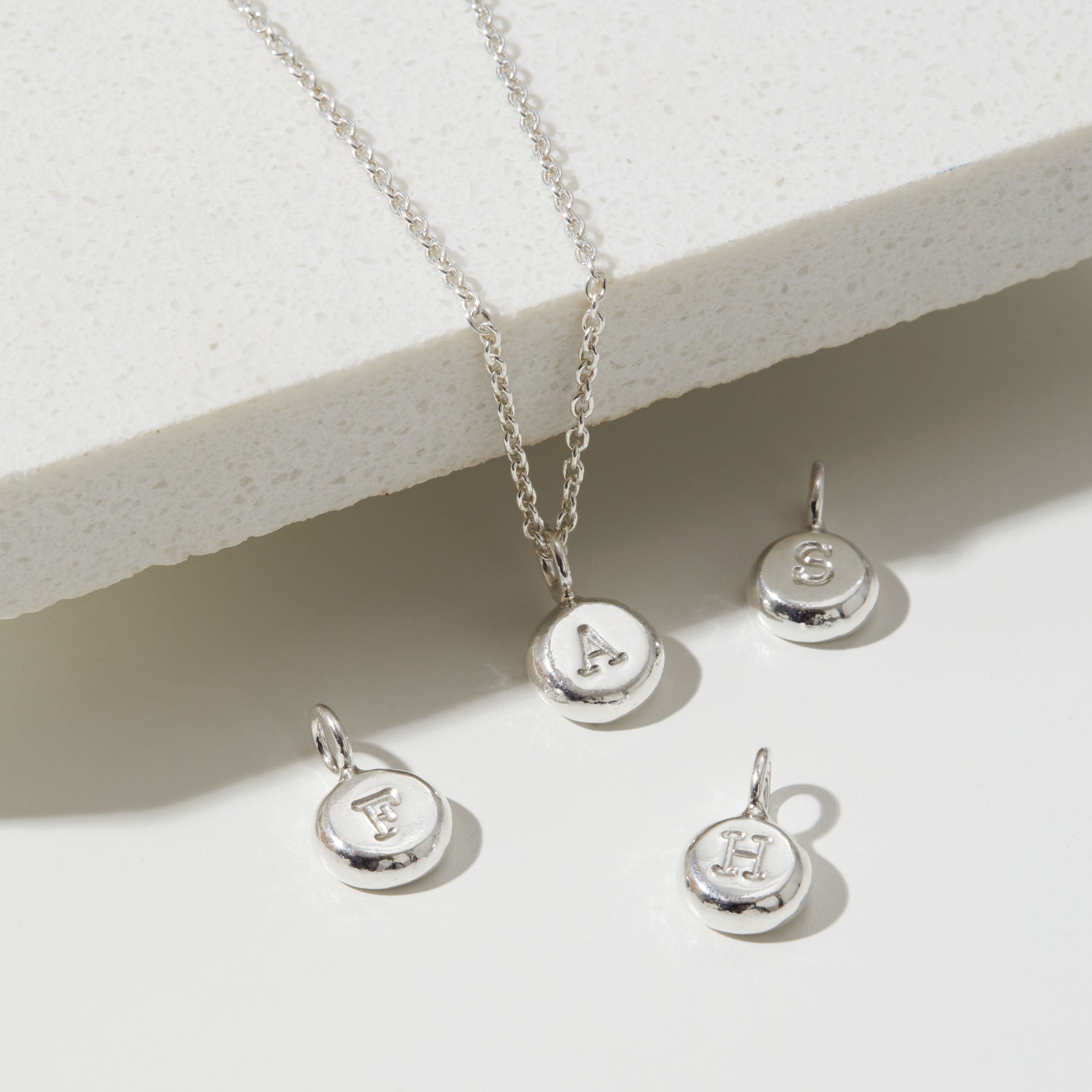 Silver necklace with letter pendants on a light background